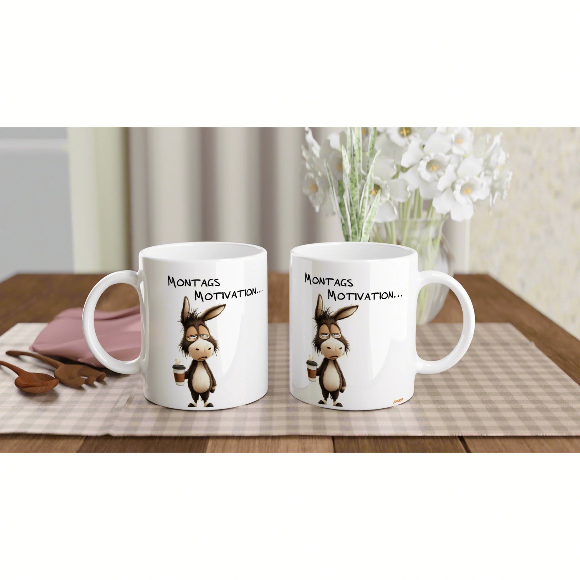Two white mugs featuring a cartoon donkey and Montags Motivation... text on a wooden table with a plaid mat and flowers.