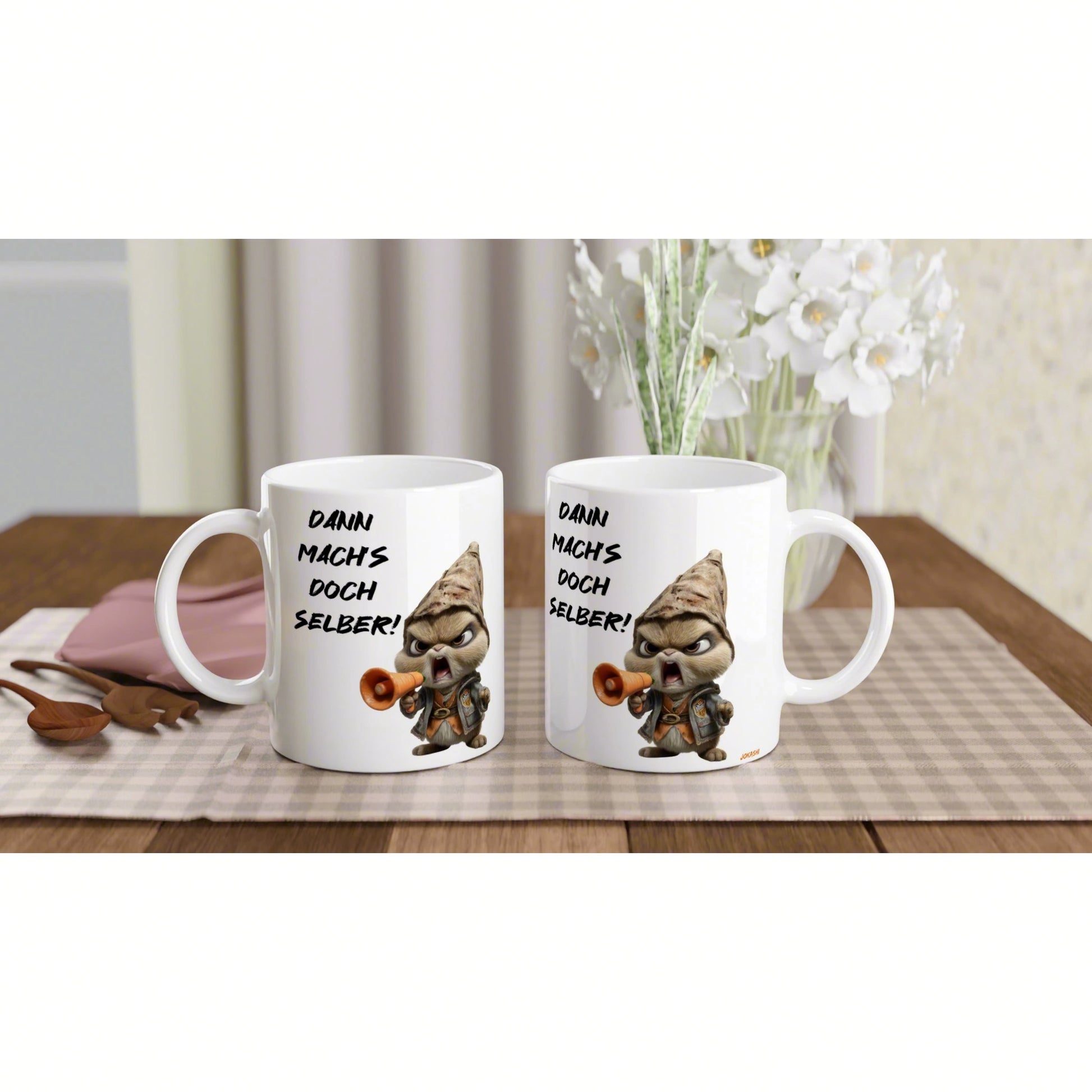 Two white mugs with a cartoon gnome and megaphone, displaying Dann machs doch selber! on a checkered placemat.