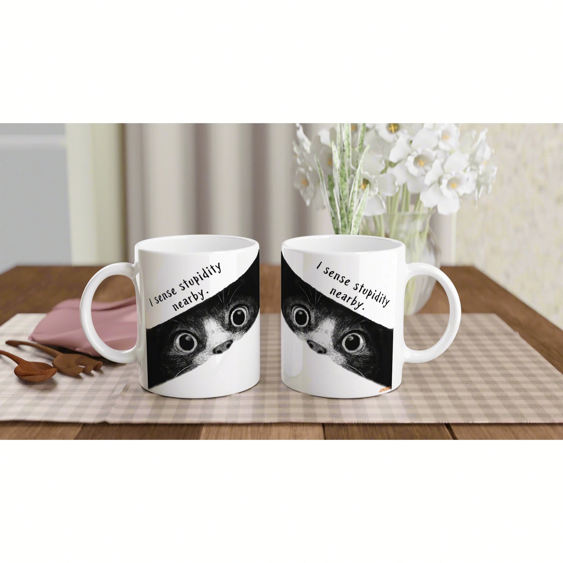 Two white mugs on a wooden table feature a black-and-white cat graphic and the caption I sense stupidity nearby.