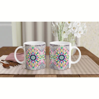 Two white mugs with colorful mandala patterns sit on a checkered placemat on a wooden table, with a vase of white flowers.