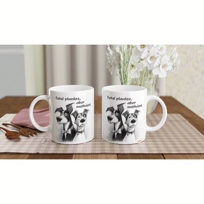 Two white mugs with a black-and-white dog cartoon and the German caption 'Total planlos, aber motiviert,' on a wooden table with flowers.