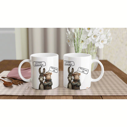 Two white mugs feature a donkey and a monkey cartoon with German speech bubbles, set on a checkered table runner.