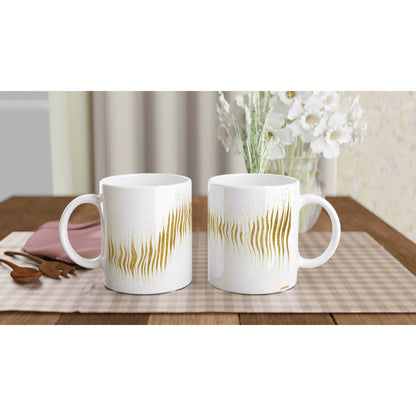 Two white ceramic mugs with gold abstract stripes on a plaid napkin, on a wooden table, with white flowers in the background.