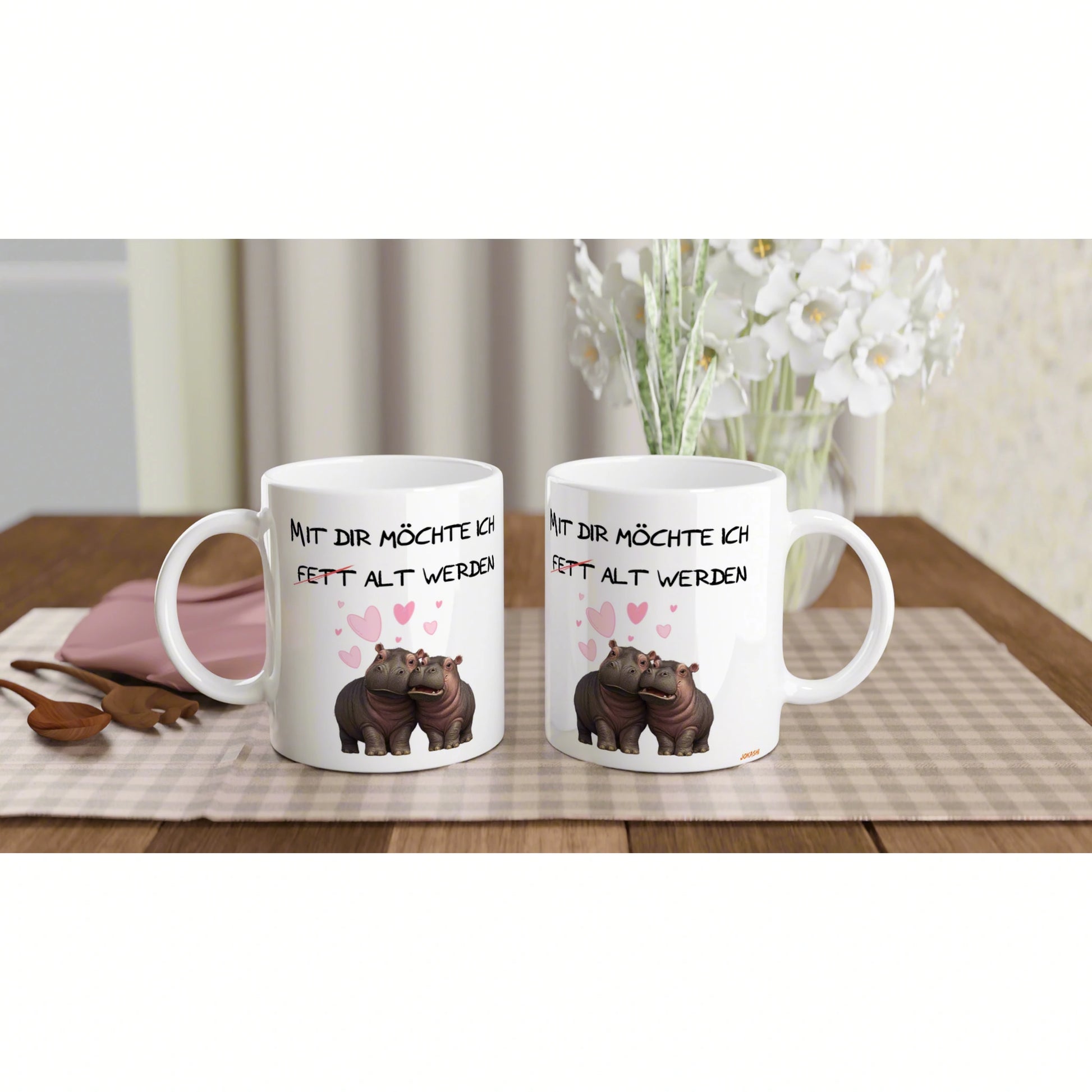 Two white mugs on a wooden table with cartoon hippos and pink hearts; product mockup for novelty cups with a German slogan.