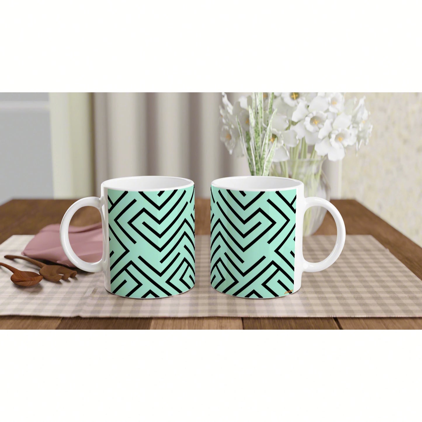 Product mockup: two white mugs with mint-green geometric maze pattern on a checkered placemat in a cozy dining scene.