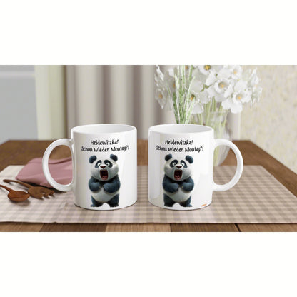Two white ceramic mugs with panda illustration and the German caption Heidewitzka! Schon wieder Montag?! on a wooden table.