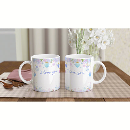 Two white mugs with pastel heart garlands and the text I love you, placed on a checkered placemat beside white flowers.