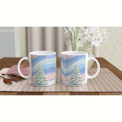 Two white mugs show a pastel winter landscape design on a wooden table; snow-covered trees and a colorful striped sky.