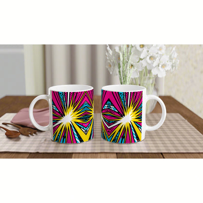 Two white mugs with pink, yellow and cyan starburst pattern on a checkered placemat, with white flowers in the background.