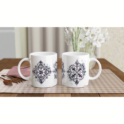Two white ceramic mugs with purple ornate medallion designs on a wooden table; vase of white flowers visible in background.