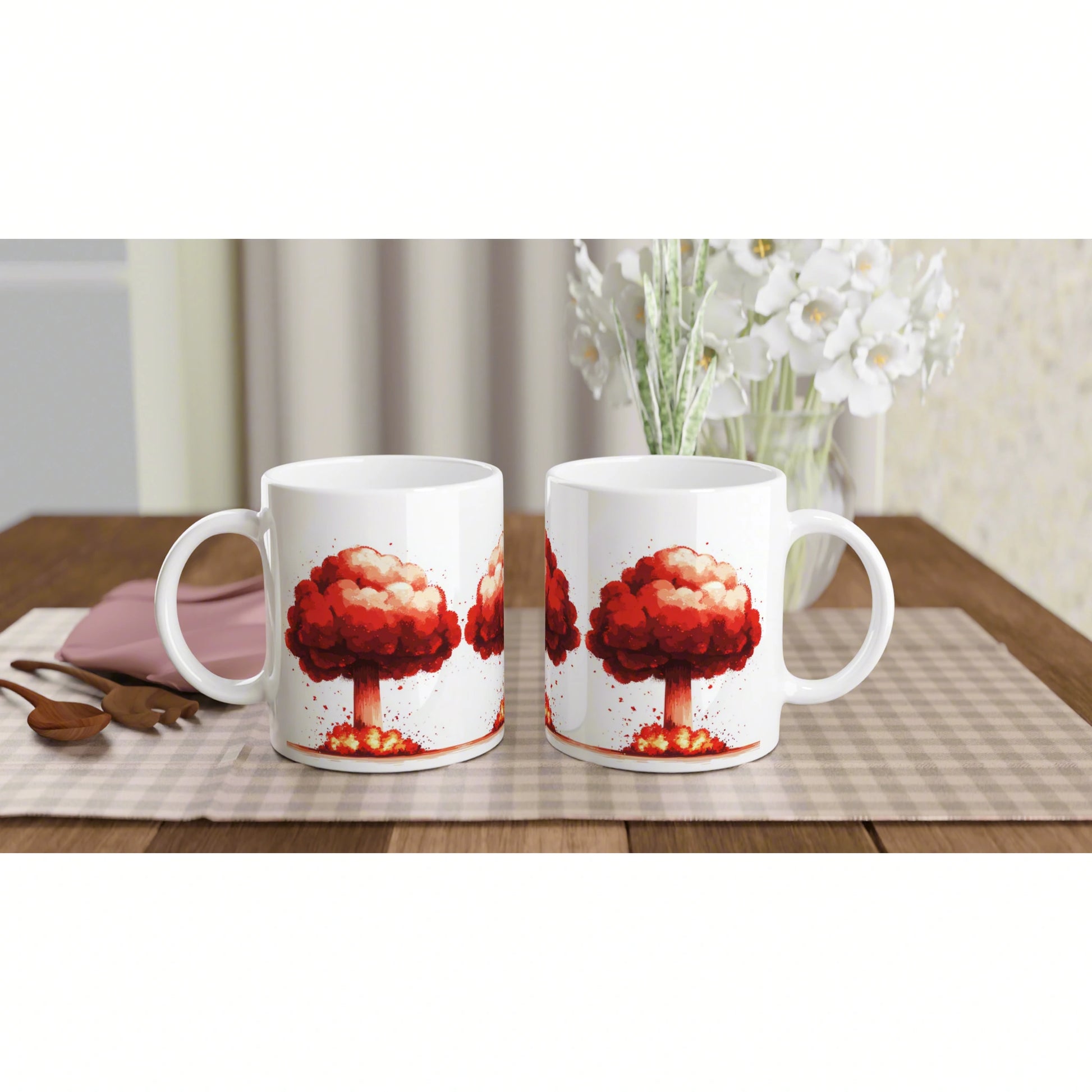 Two white mugs with a red tree artwork sit on a wooden table, with a vase of white flowers in the background.