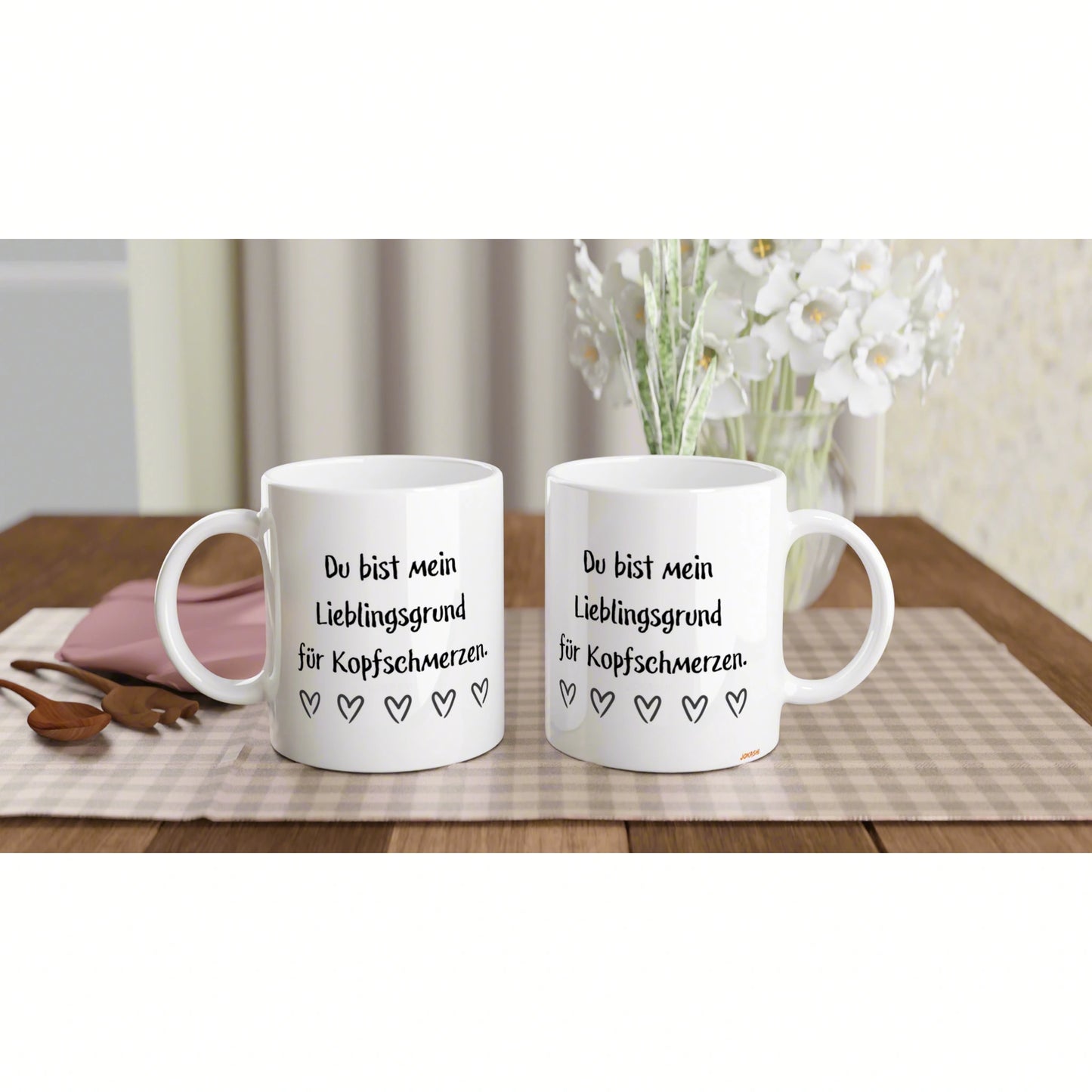 Two white mugs on a wooden table with a vase; product mockup showing the slogan 'Du bist mein Lieblingsgrund für Kopfschmerzen' and small hearts.