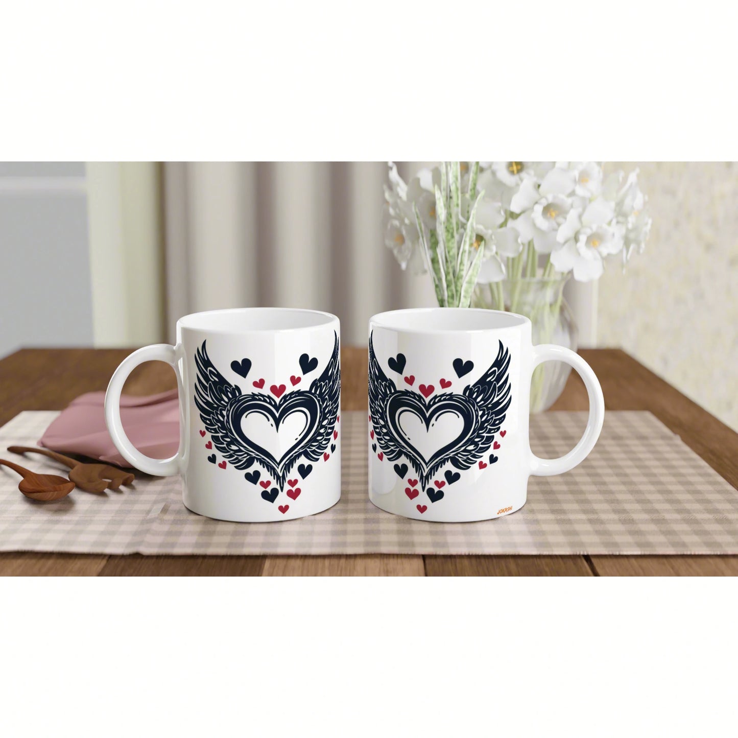 Product mockup: two white mugs with a black winged-heart design and small red hearts on a wooden table.