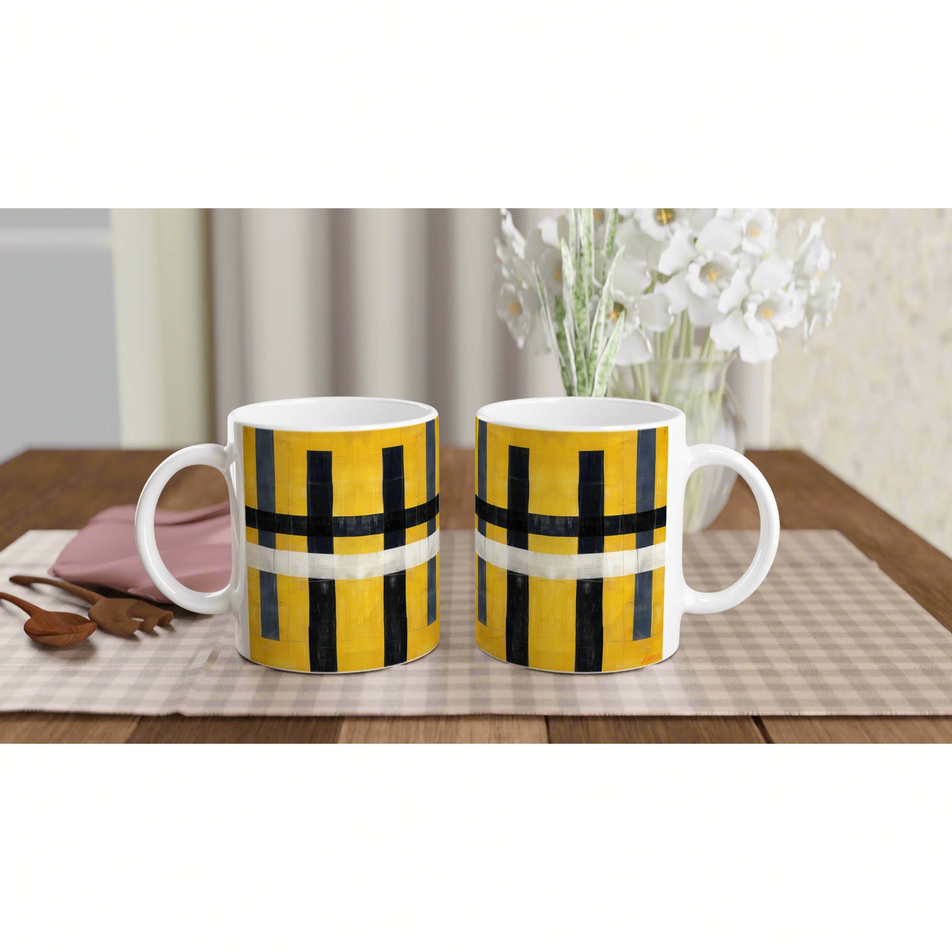 Two yellow and black geometric mugs on a beige checkered table runner, with white flowers in the background.