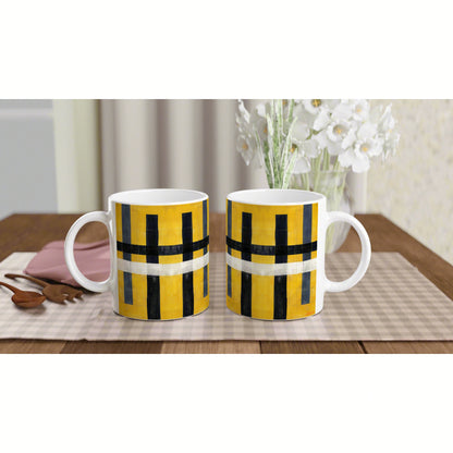 Two yellow and black geometric mugs on a beige checkered table runner, with white flowers in the background.