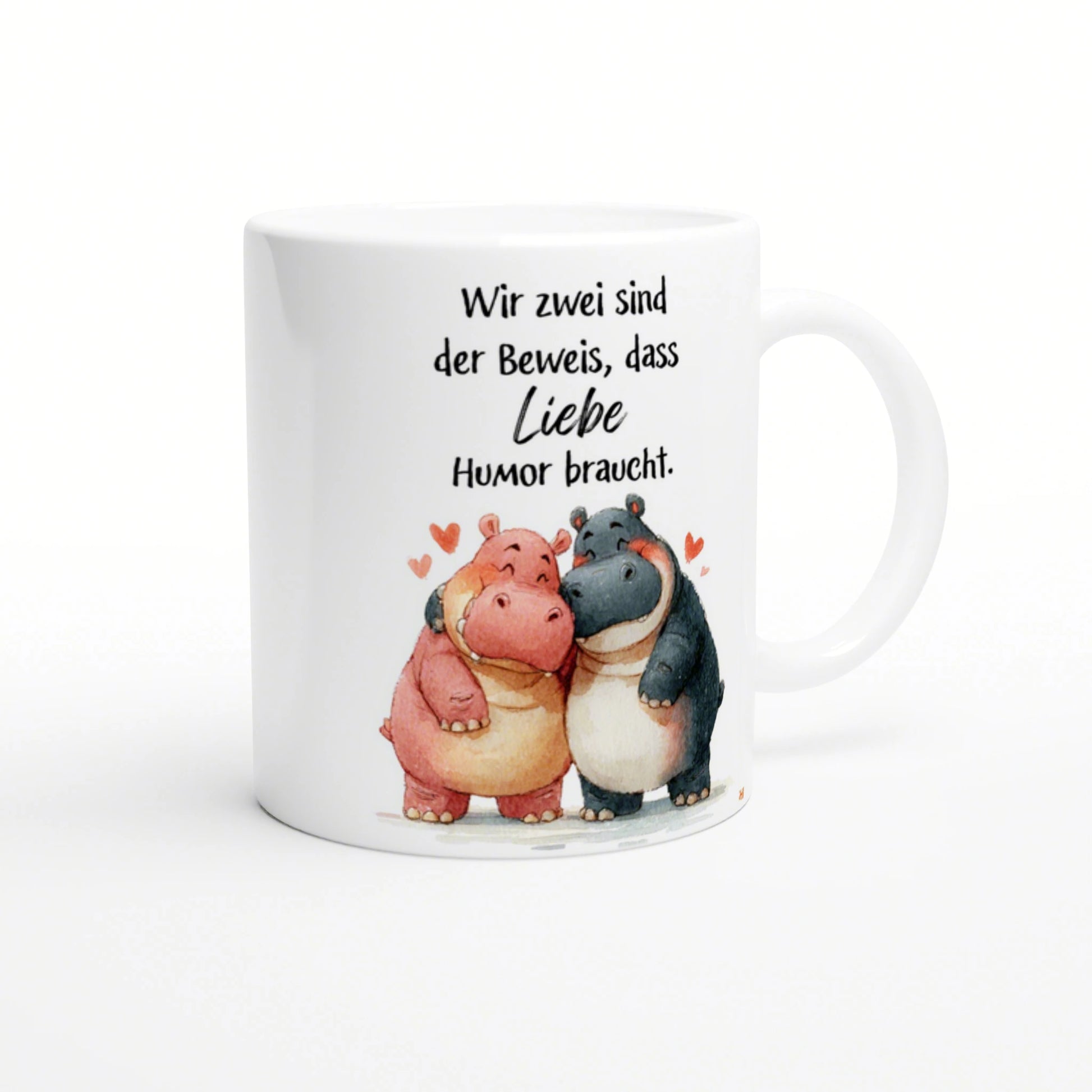 Weiße Kaffeetasse mit zwei cartoon-Nilpferden, die sich umarmen, und dem Spruch 'Liebe braucht Humor'.
