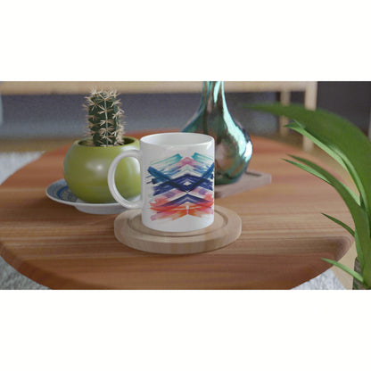 White ceramic mug with a vibrant multicolor abstract chevron brushstroke pattern on a wooden table, surrounded by plants.