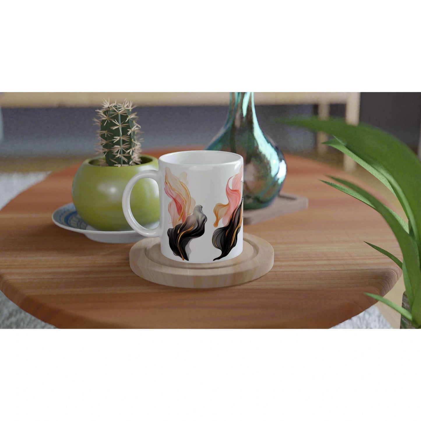 White ceramic mug with an abstract pink, orange, and black flowing floral design on a wood table beside a cactus and vase.