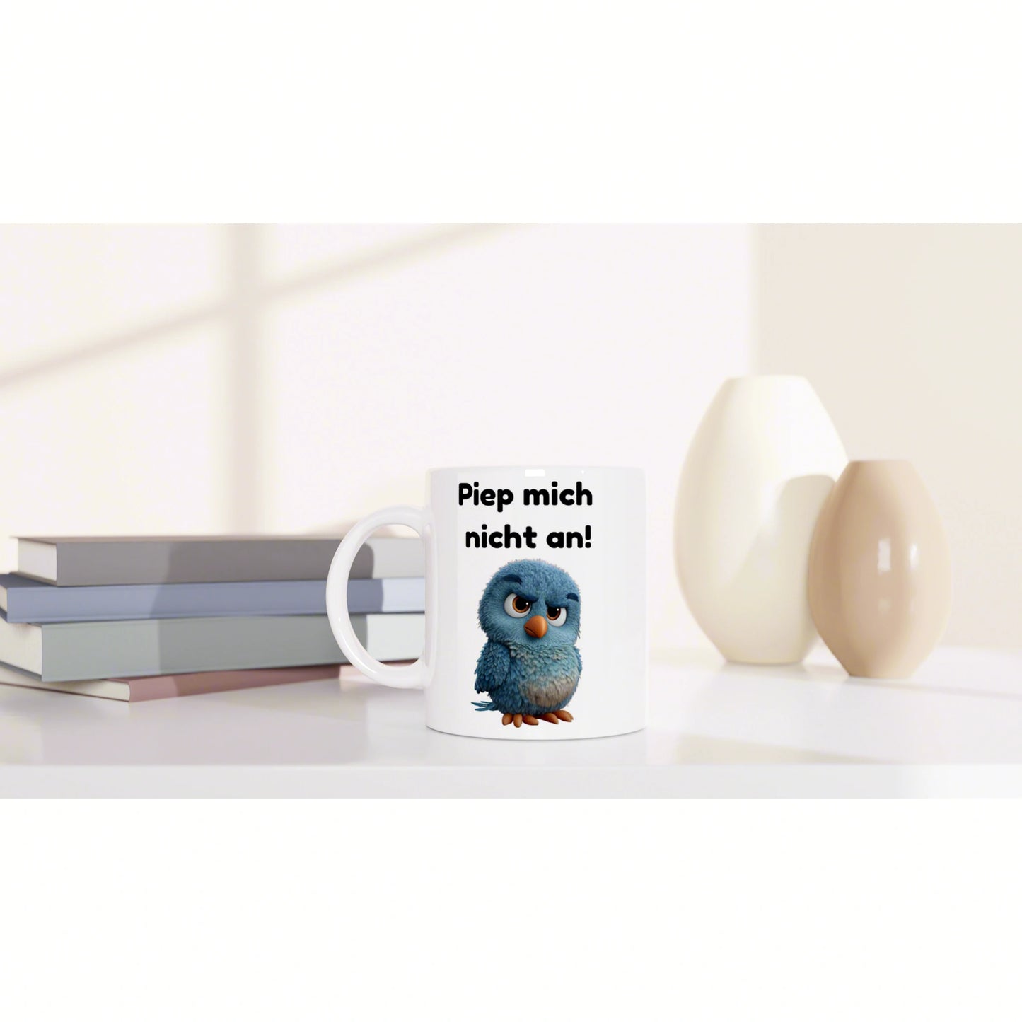 White ceramic mug featuring a blue cartoon bird and the text 'Piep mich nicht an!' on a clean desk with books and vases.