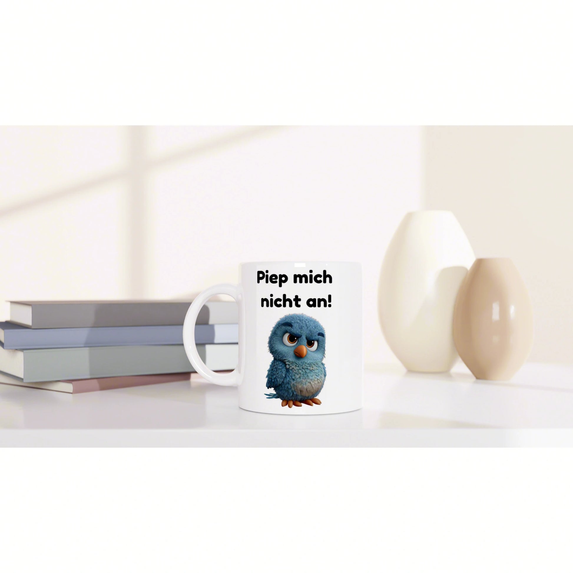 White ceramic mug featuring a blue cartoon bird and the text 'Piep mich nicht an!' on a clean desk with books and vases.
