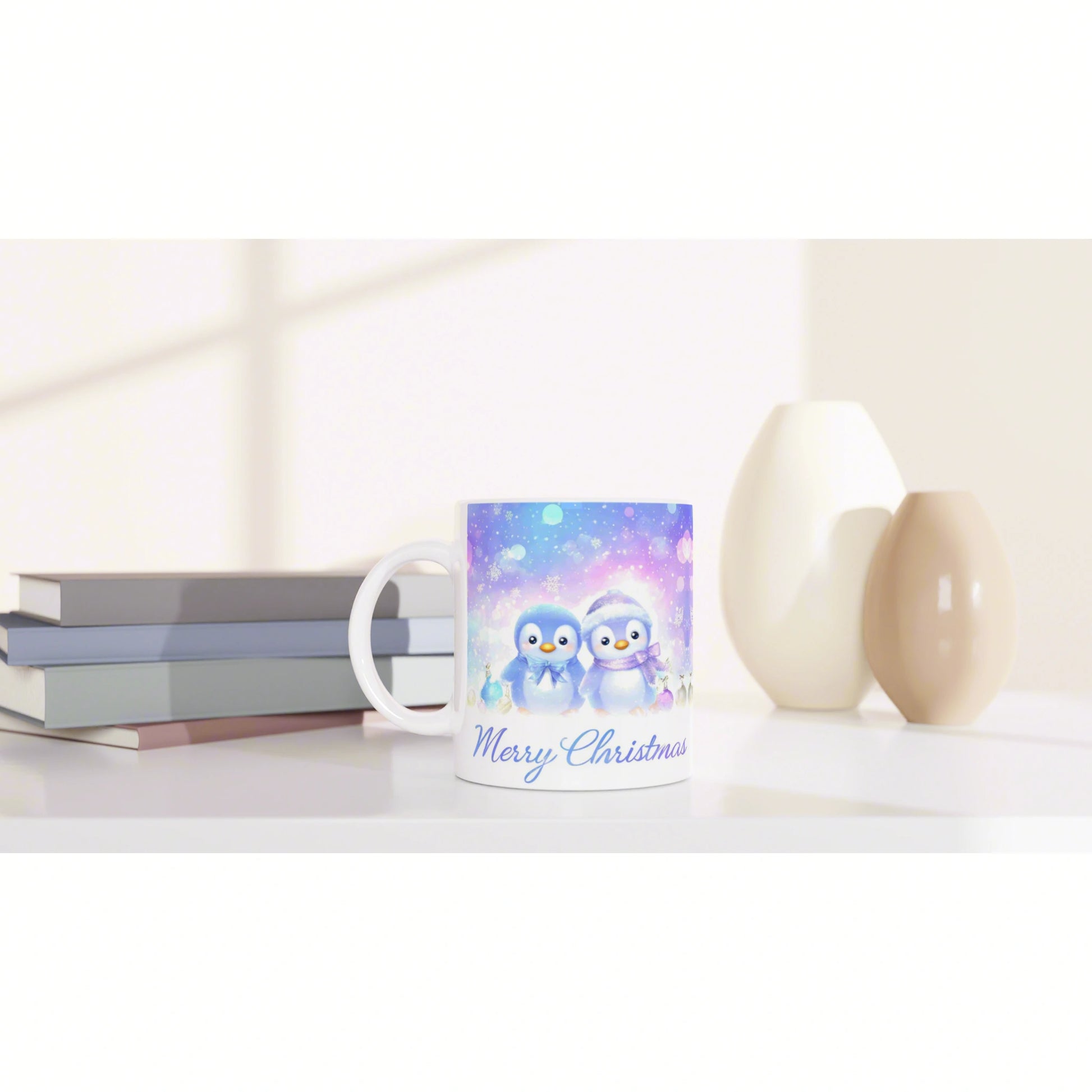 White ceramic mug with blue penguin illustration and Merry Christmas text, shown as a product mockup beside books and vases.