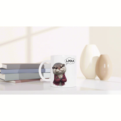 White ceramic mug with a cartoon animal in a red hoodie and a 'LMAA' thought bubble, placed on a shelf with books and vases.