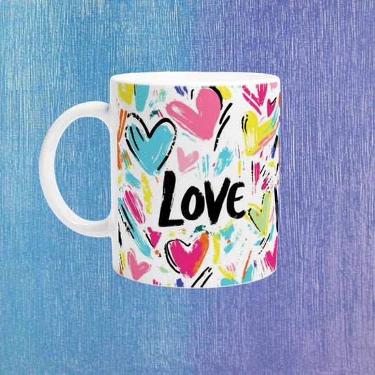 White ceramic mug featuring colorful brush-stroke hearts and the bold LOVE text, on a blue textured backdrop.