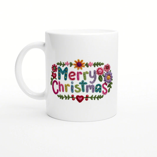 White ceramic mug with a colorful embroidered 'Merry Christmas' design and a floral border.