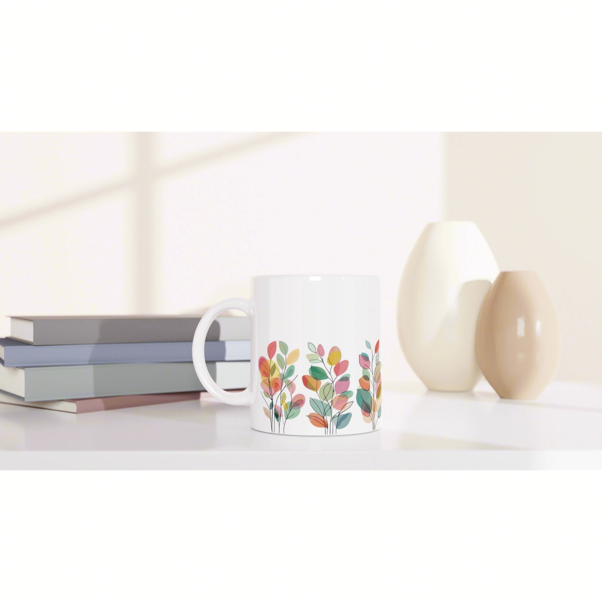 White ceramic mug with a colorful leafy botanical pattern on a white shelf beside stacked books and cream vases.