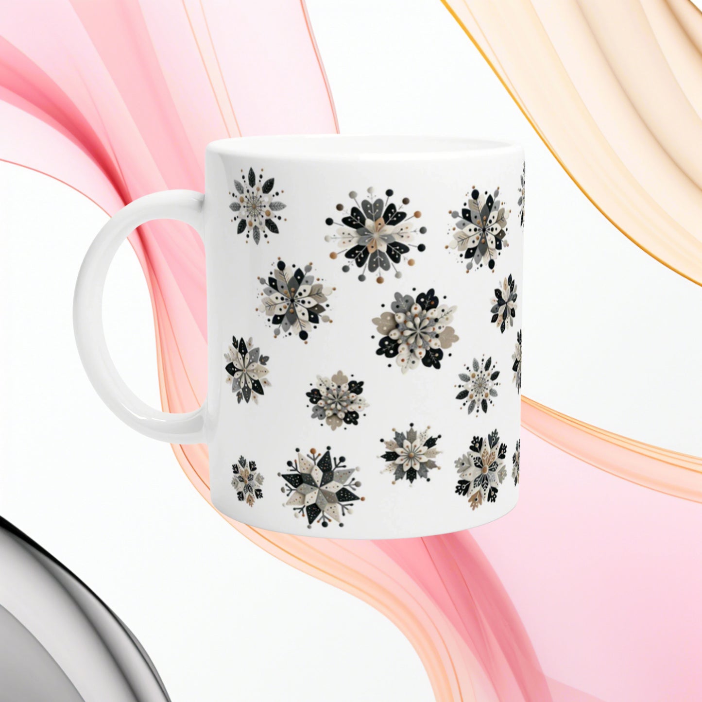 White ceramic mug with black-gray floral snowflake pattern; pink and peach ribbon backdrop, product mockup.