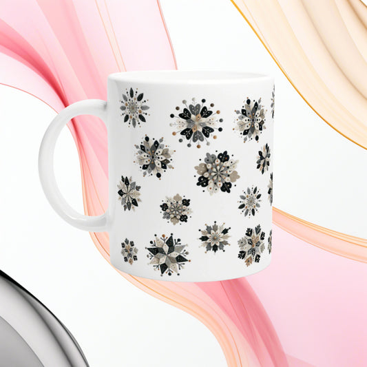 White ceramic mug with black-gray floral snowflake pattern; pink and peach ribbon backdrop, product mockup.