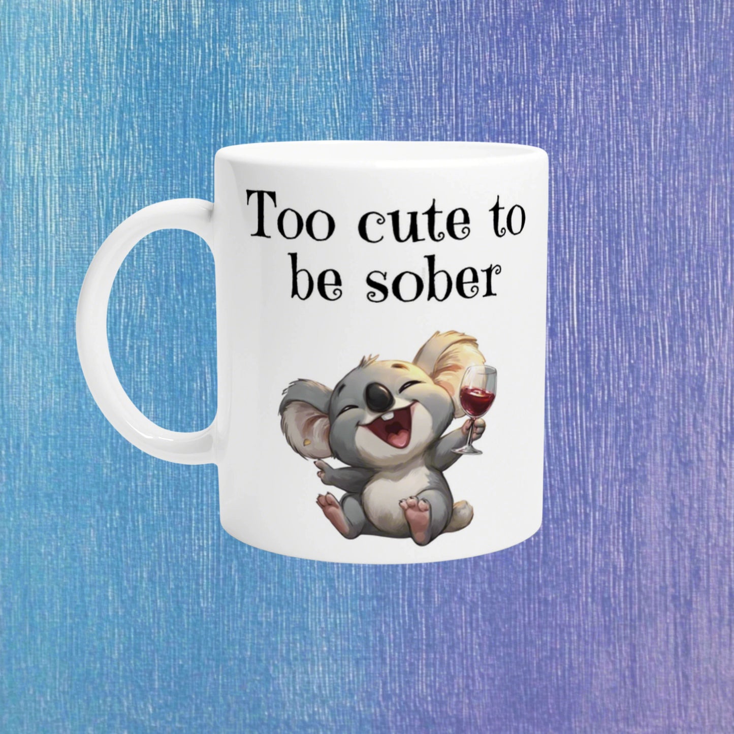 White ceramic mug featuring a laughing koala holding a wine glass and the slogan 'Too cute to be sober'.
