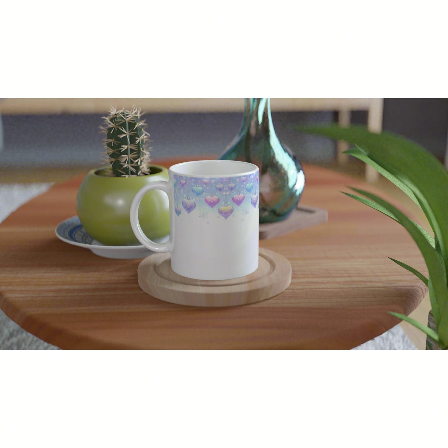 White ceramic mug with pastel heart pattern on a wooden coaster, on a wooden table beside a cactus pot and teal vase.