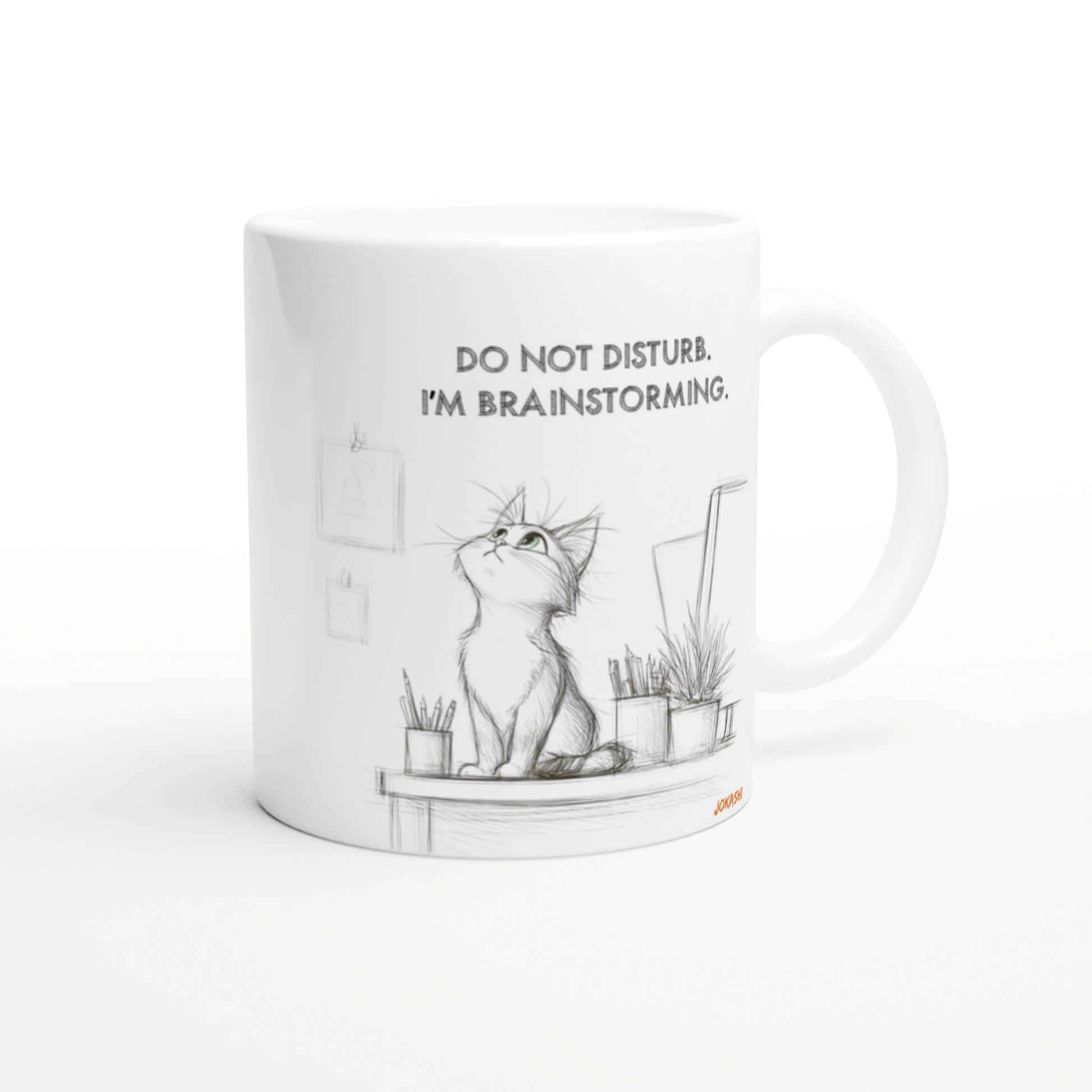 White ceramic mug with a pencil sketch of a cat on a desk, surrounded by plants, captioned Do not disturb. I'm brainstorming.