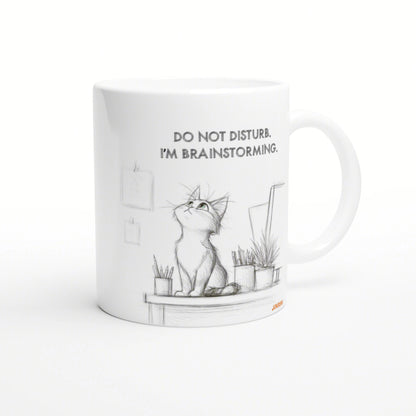 White ceramic mug with a pencil sketch of a cat on a desk, surrounded by plants, captioned Do not disturb. I'm brainstorming.