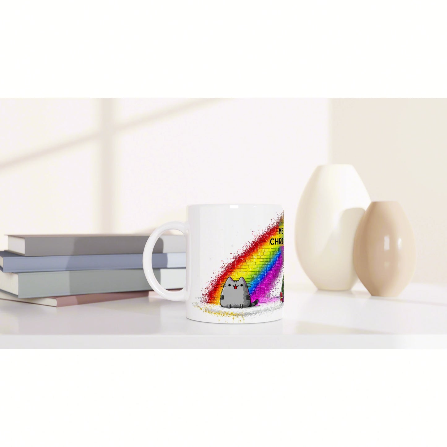 White ceramic mug with a rainbow paint-splash design and a cute gray cat, set on a desk with books and vases; product mockup.