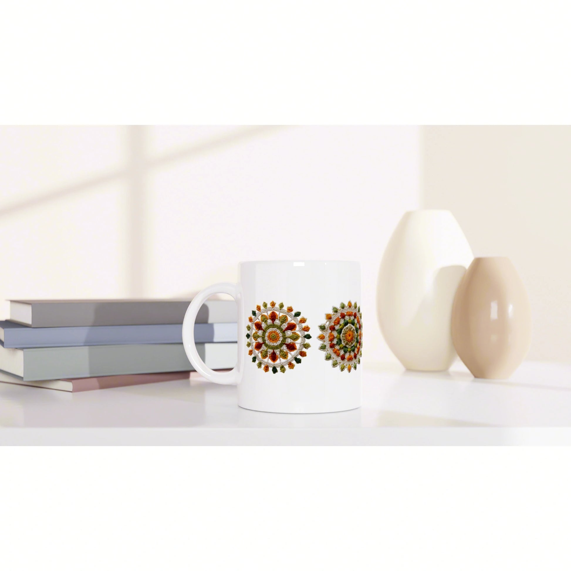 White ceramic mug with two colorful circular mandala designs, placed on a shelf beside stacked books and decorative vases.