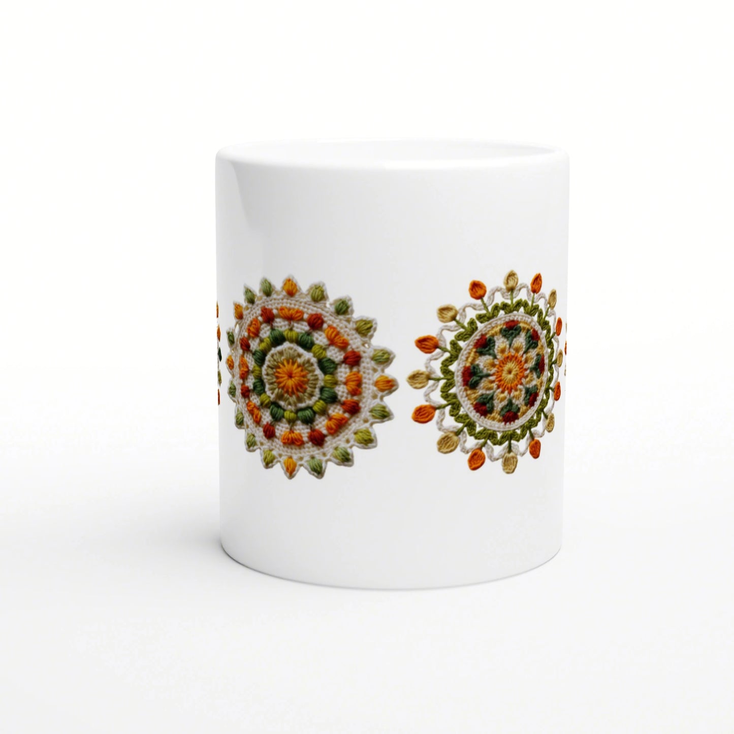 White ceramic mug on a white background featuring two colorful crocheted mandala designs in orange, green and yellow.