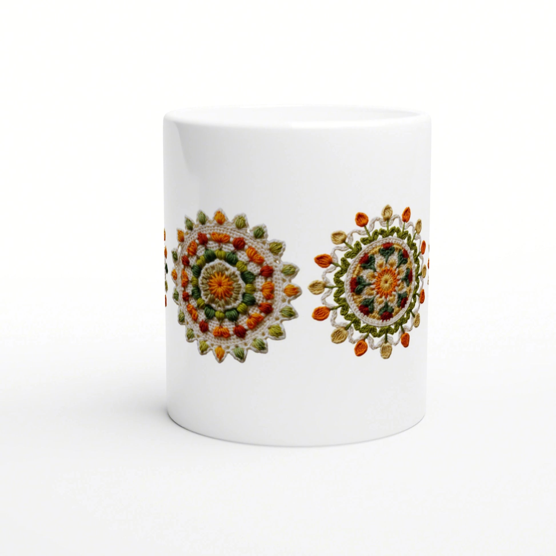 White ceramic mug on a white background featuring two colorful crocheted mandala designs in orange, green and yellow.