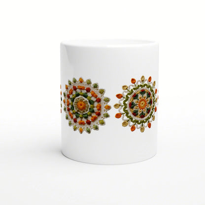 White ceramic mug on a white background featuring two colorful crocheted mandala designs in orange, green and yellow.