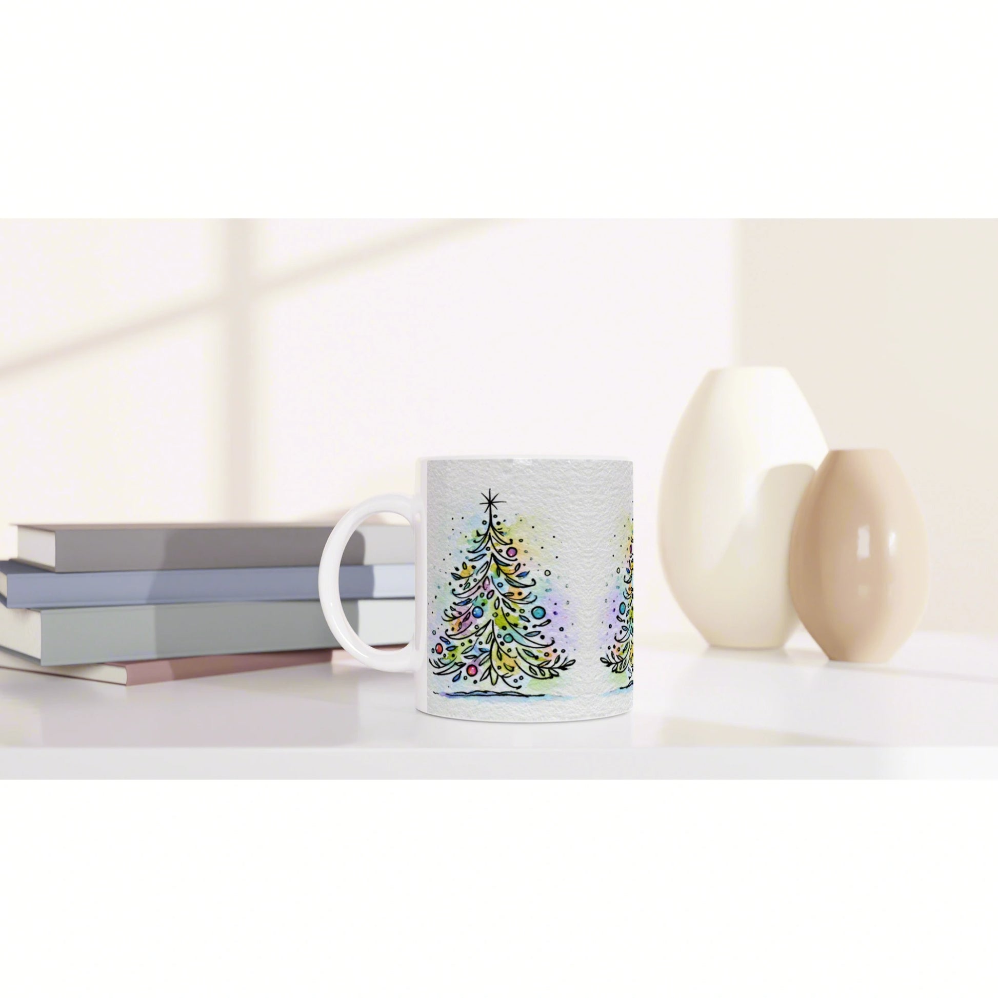 White ceramic mug with colorful watercolor Christmas tree design on a desk beside books and decorative vases.