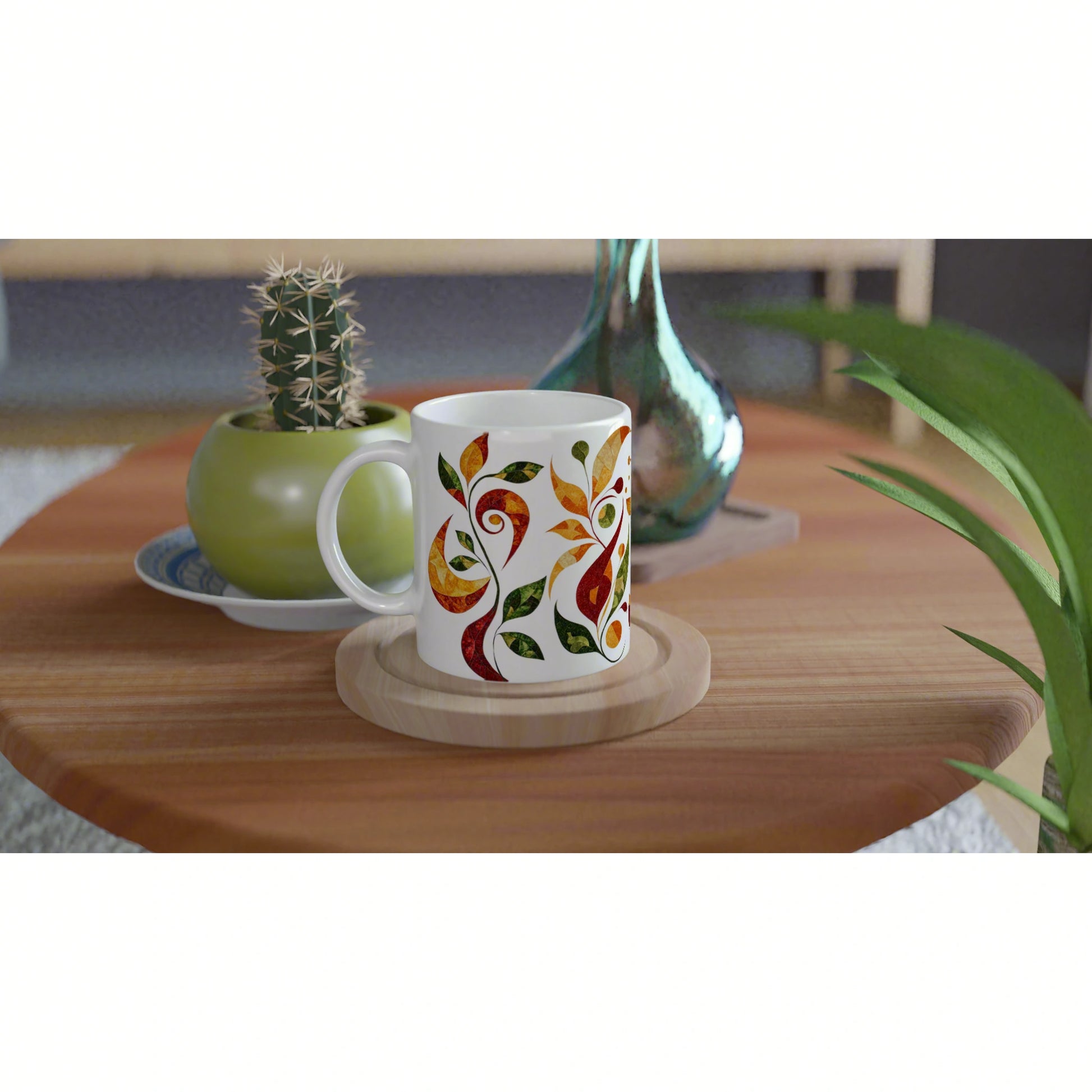 White mug featuring colorful abstract floral design on a wooden coaster, on a table with a potted cactus and a glass vase.