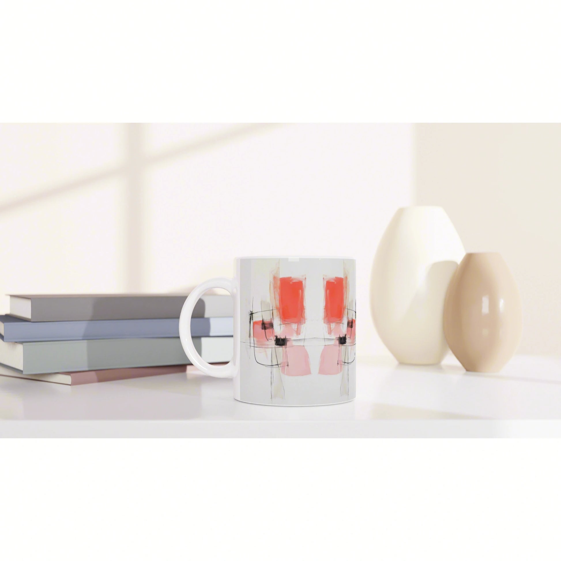 White ceramic mug with an abstract pink and red pattern and black lines, on a desk beside stacked books and cream vases.