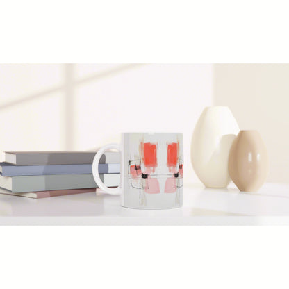 White ceramic mug with an abstract pink and red pattern and black lines, on a desk beside stacked books and cream vases.