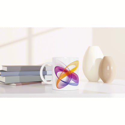 White mug with a vibrant abstract swirl in orange, purple and blue, set on a desk beside books and ceramic vases