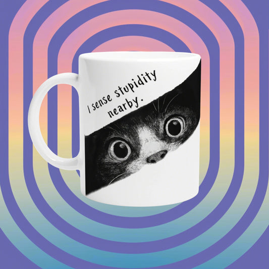 White mug showing a black-and-white animal face with the caption 'I sense stupidity nearby' on a diagonal panel, against a retro rainbow gradient.