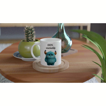 White mug featuring a blue fluffy monster and the text 100% unschuldig, on a wooden table with potted plants nearby.