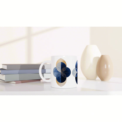 White mug featuring a blue and gold geometric quatrefoil flower design, beside pastel books and cream vases.
