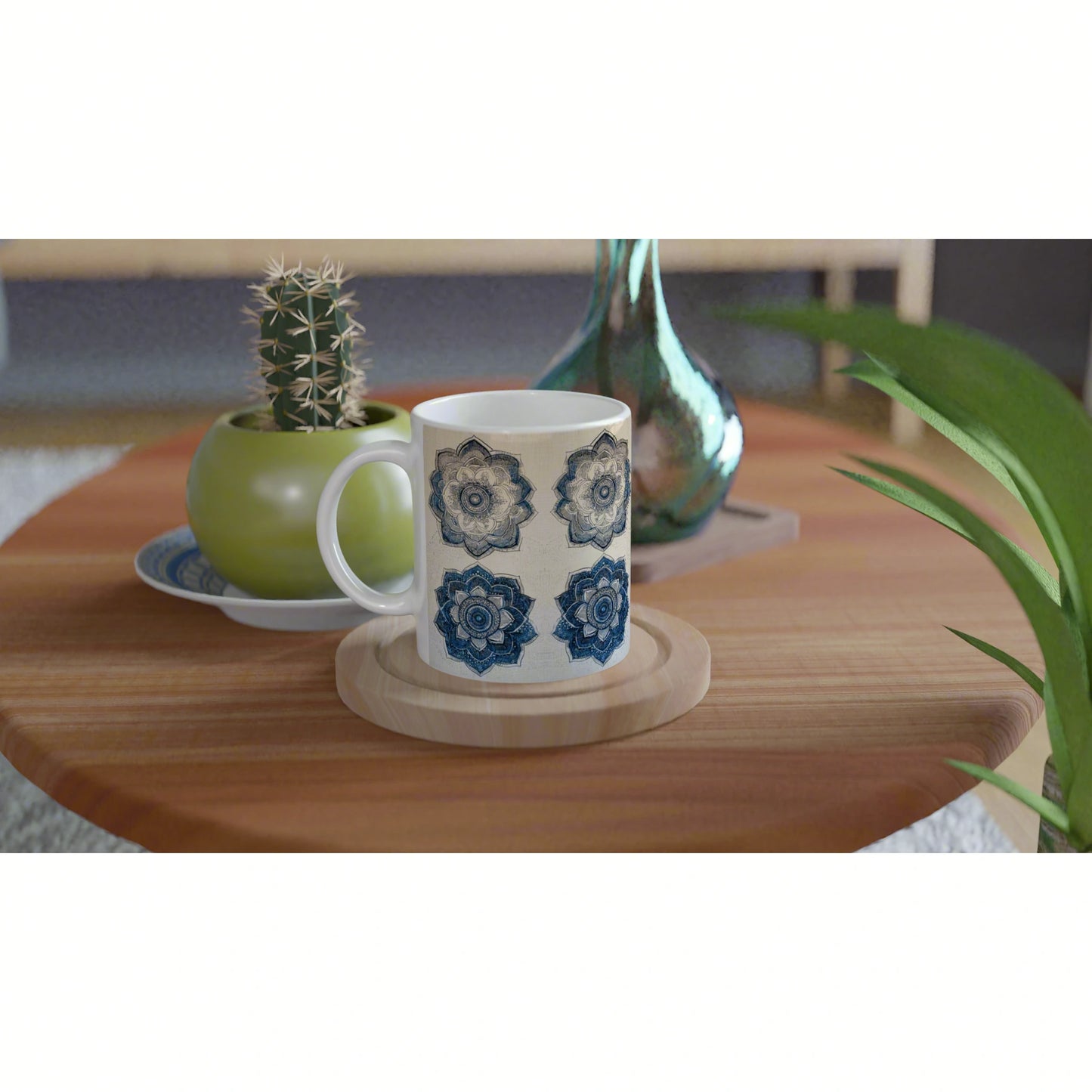 White mug with blue mandala designs on a wooden coaster, on a warm table with a potted cactus and decorative vase nearby.