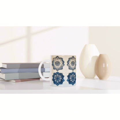 White mug with blue mandala pattern sits on a white desk beside stacked books and beige ceramic vases; a product mockup.